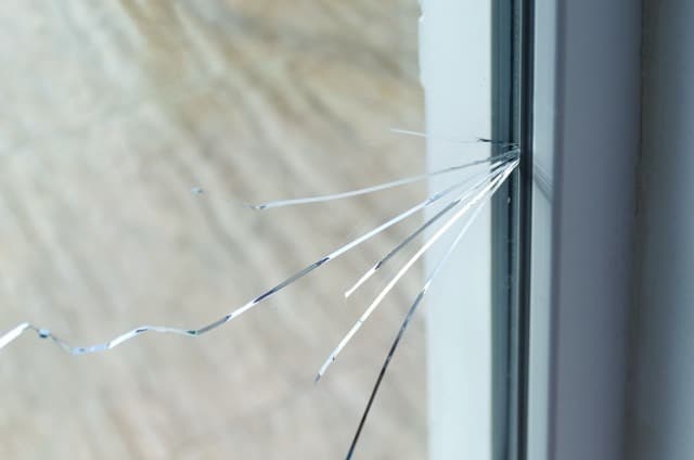 A damaged window with broken glass and a fractured frame, illustrating a state of disrepair and potential safety hazard.