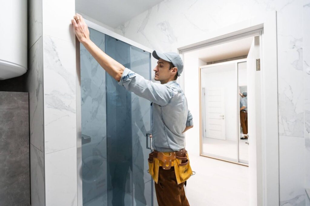 A man in a blue shirt and cap stands in front of a bathroom door, looking towards the camera