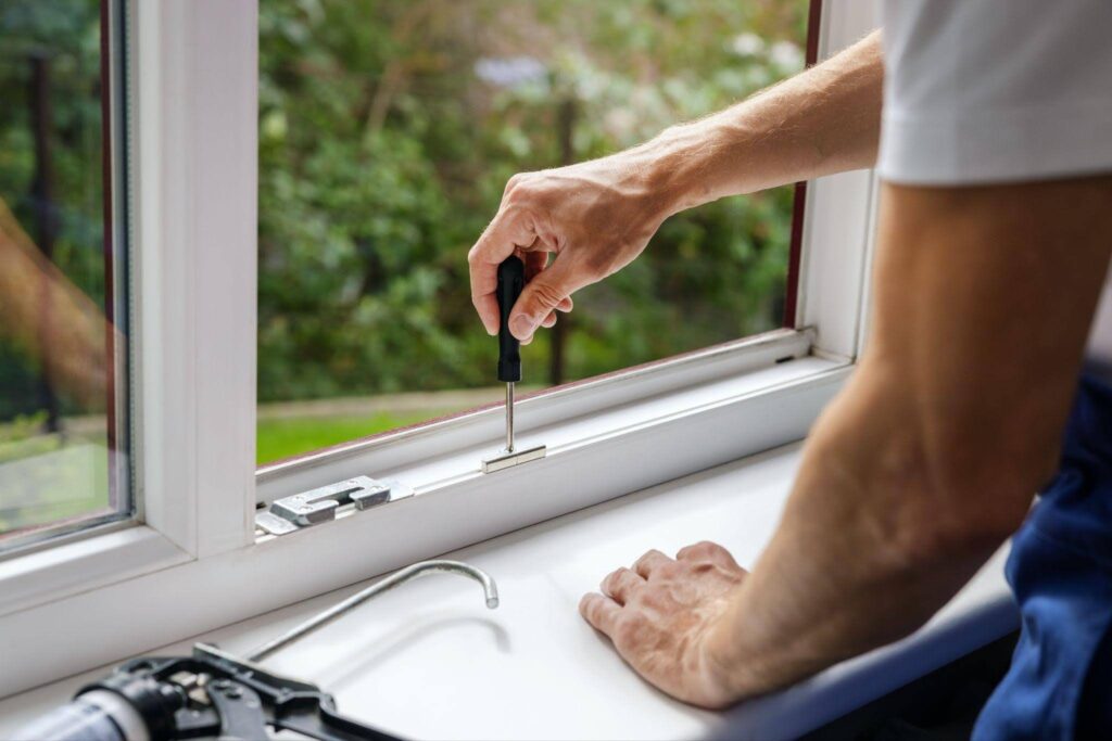 Person using a screwdriver to repair a white window frame above a sink