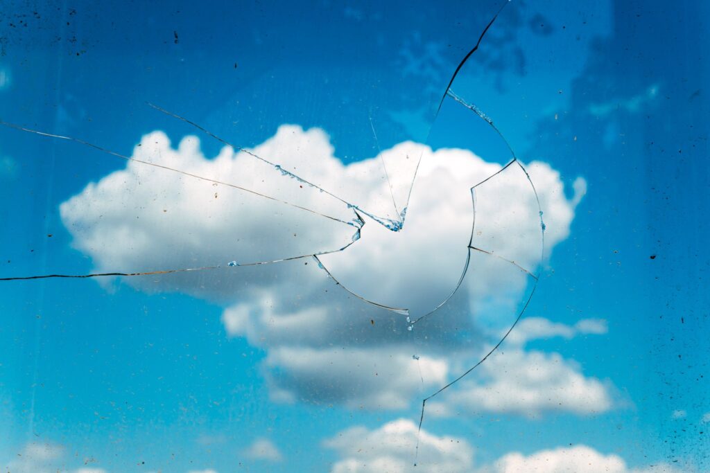 Cracked glass pane with a blue sky and white cloud visible in the background.