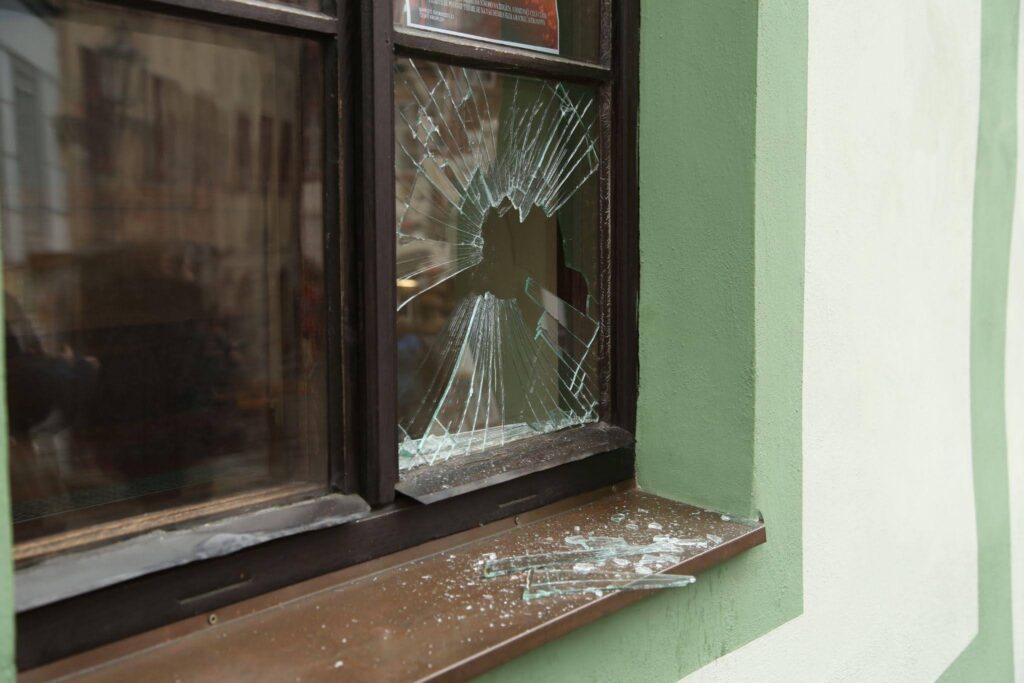 Shattered window with a large hole and radiating cracks glass scattered on the sill