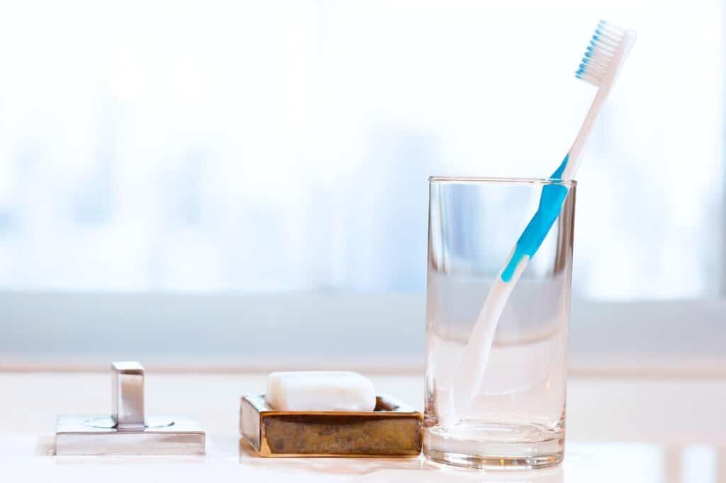 A toothbrush and a glass of water sit beside a bar of soap indicating preparation for brushing teeth
