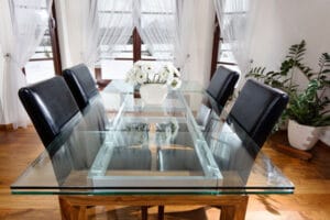 A glass dining table with four black chairs arranged around it.