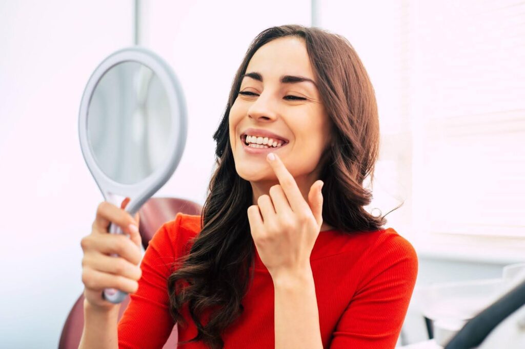 A woman looks into a mirror observing her face with a contemplative demeanor