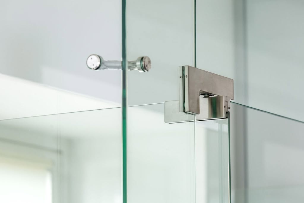 Close-up of a metal pivot hinge on a frameless glass shower door.