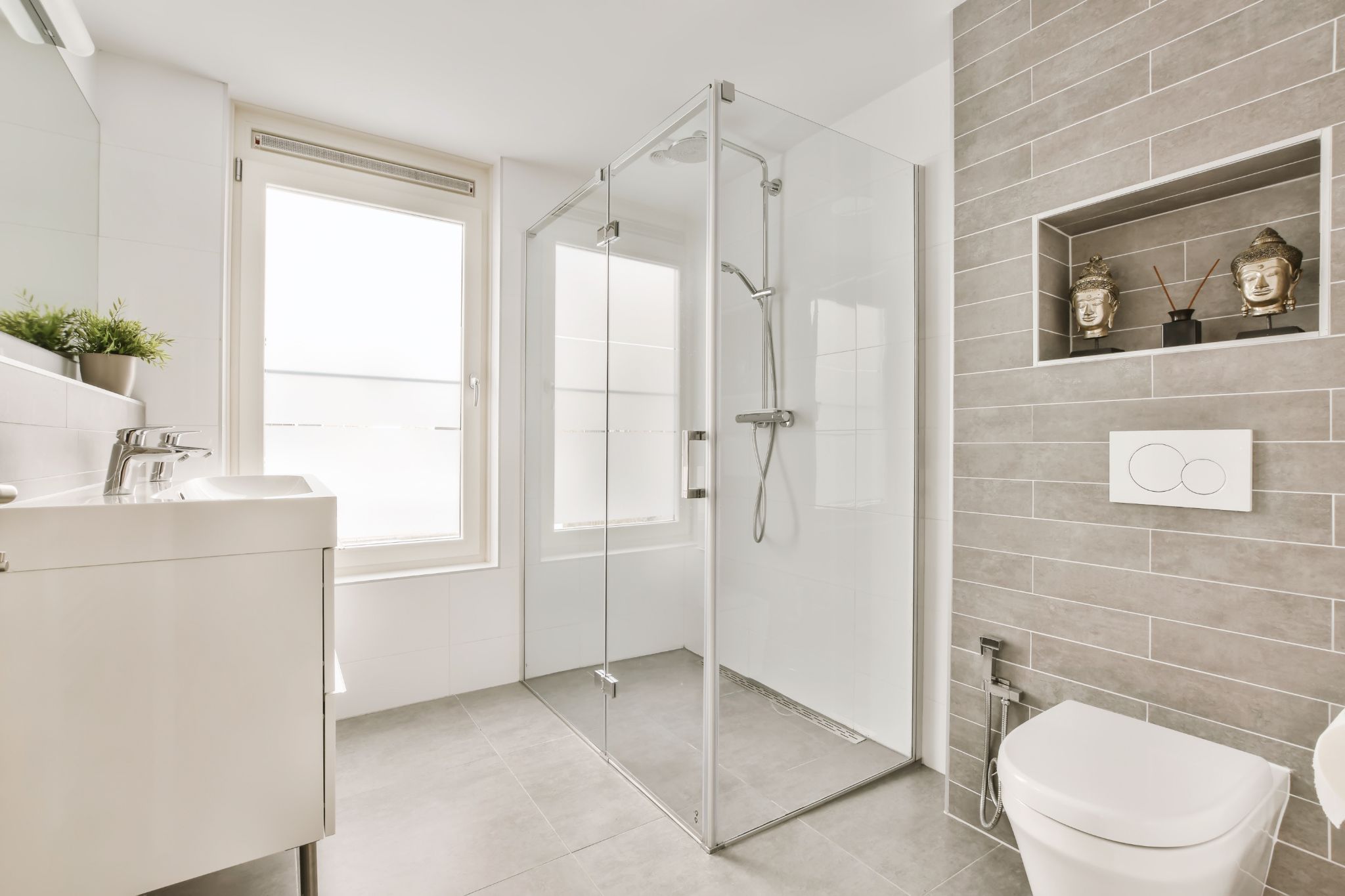 Modern bright bathroom with a glass shower enclosure, white vanity, and grey tiled wall with built-in decor niche.