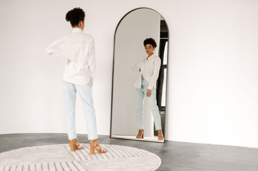 A woman in a white shirt and blue jeans standing in front of a mirror.