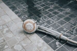 A close-up of a shower head positioned over a clean, tiled floor in a bathroom setting.