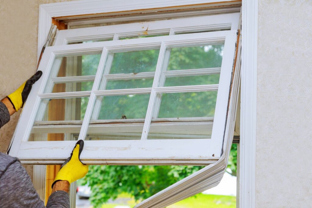A person wearing yellow gloves installing or removing a multi-paned window.