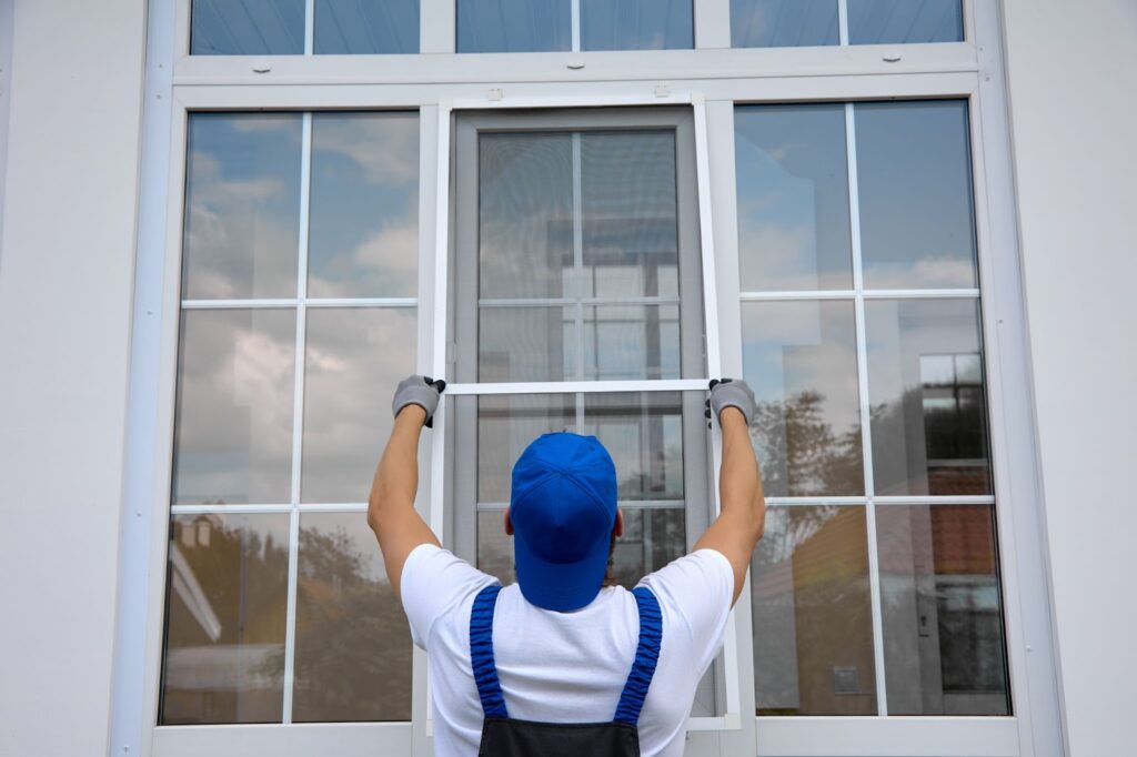 Worker installing a window screen on a large window.