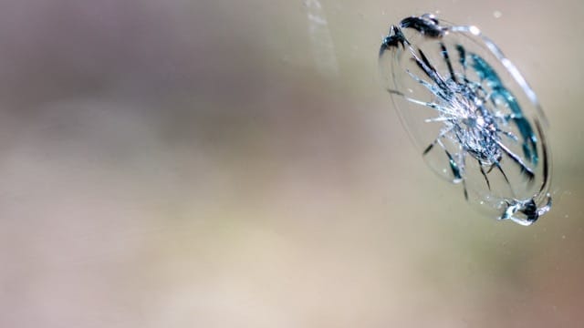 A broken glass window featuring a bullet hole, with shards scattered around the frame.