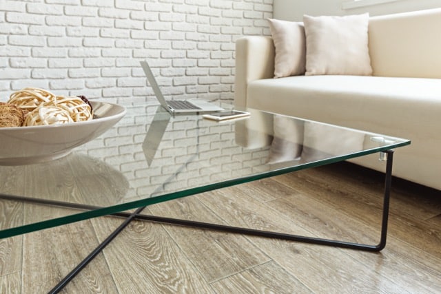 A glass coffee table featuring a laptop placed on its surface.
