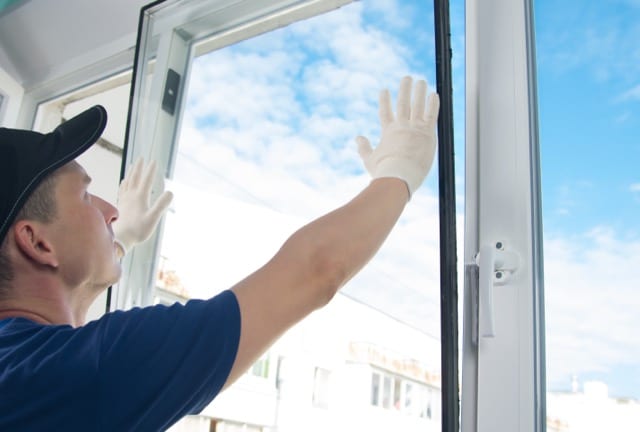 A man in a blue shirt and white gloves cleans a window, focusing on repairs and maintenance.