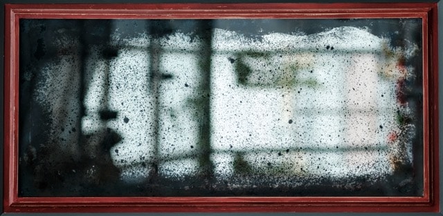 An old, tarnished mirror with heavy black spotting and a red wooden frame.