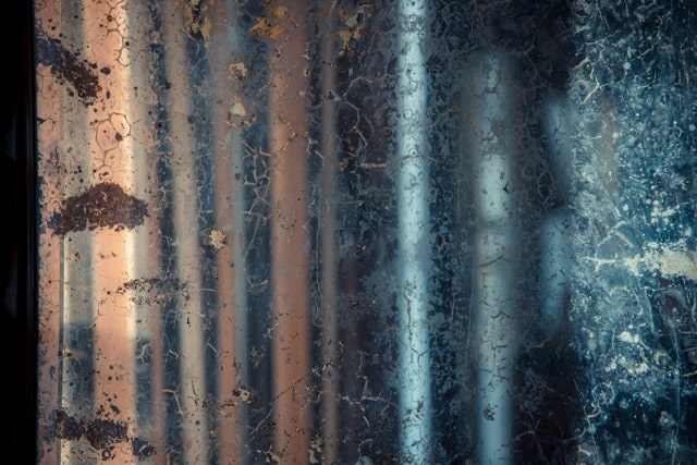 Close-up of a weathered, cracked glass pane covered in grime and rust stains