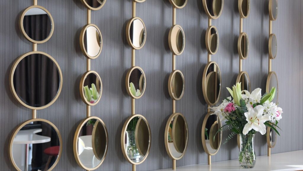 A decorative wall featuring multiple mirrors and a vibrant vase filled with fresh flowers