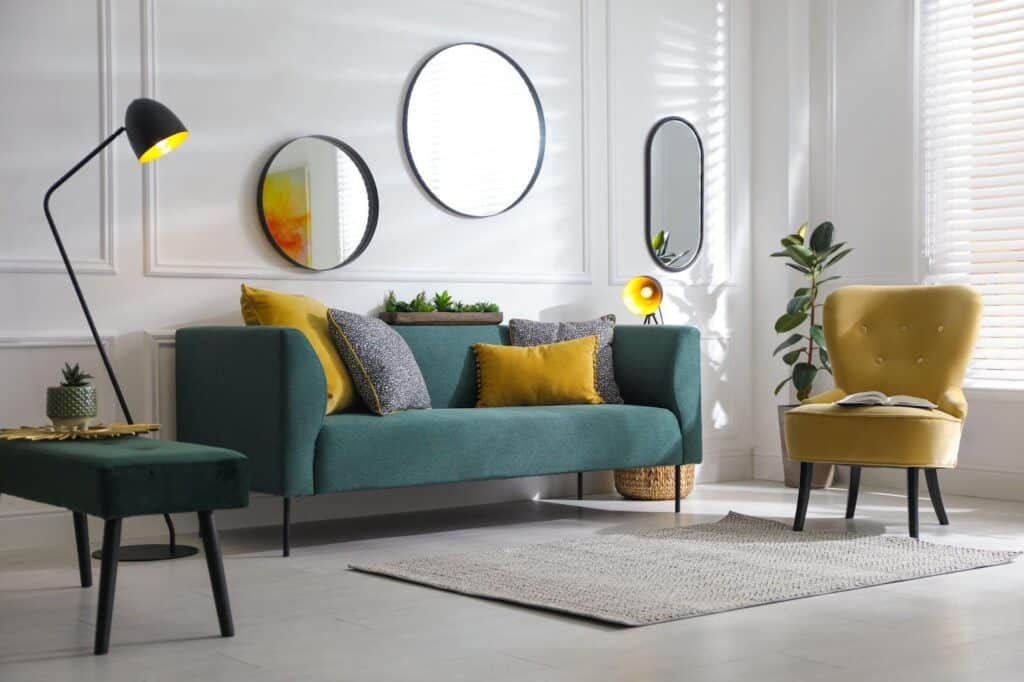 A living room featuring a green couch a yellow chair and a decorative mirror on the wall