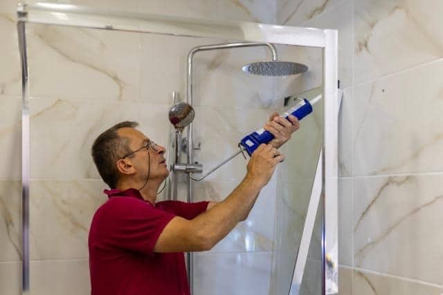 A man is using a blue cleaning tool to scrub the shower ensuring a thorough clean of the surfaces