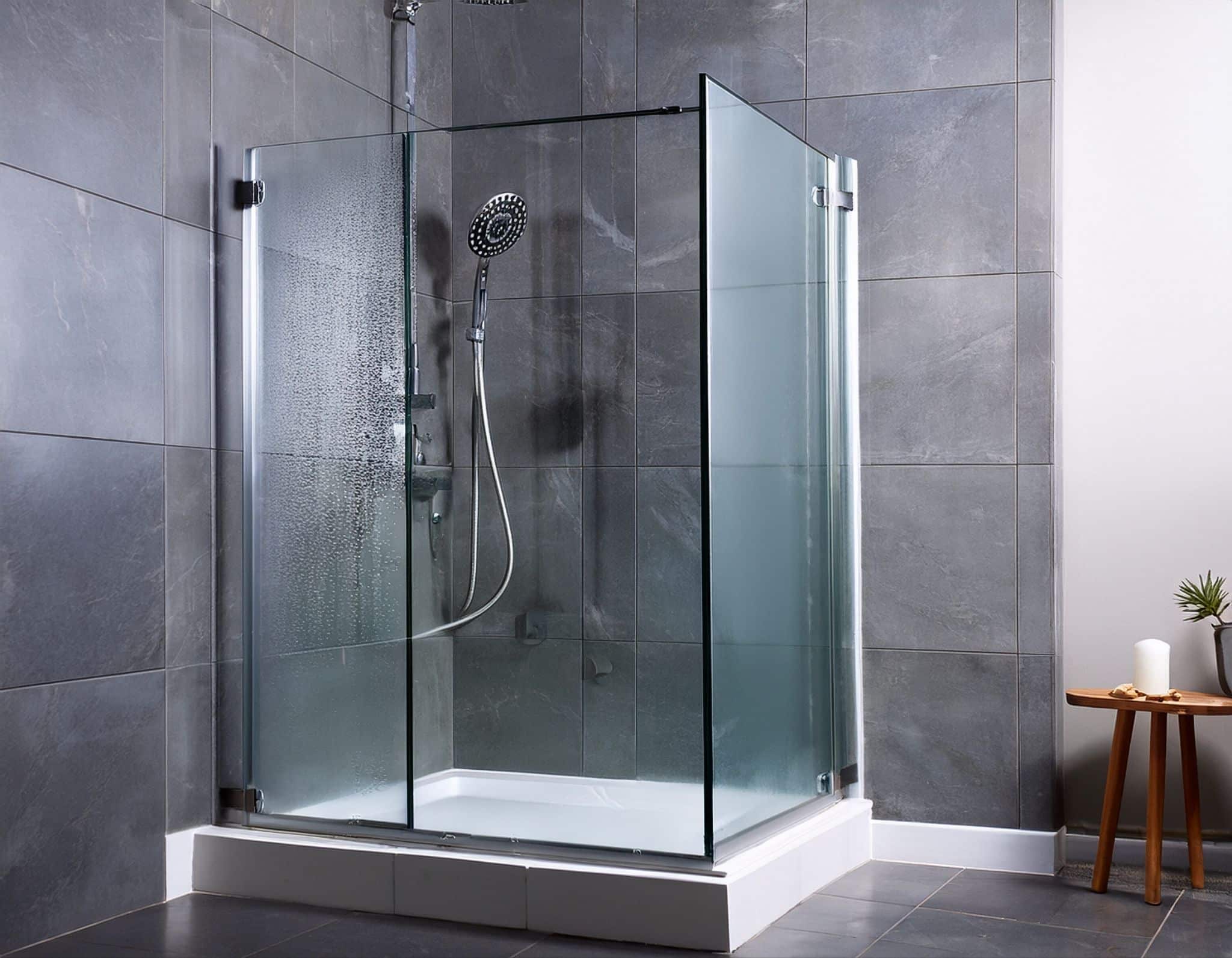 Frameless glass corner shower enclosure with gray wall tiles and white shower tray.