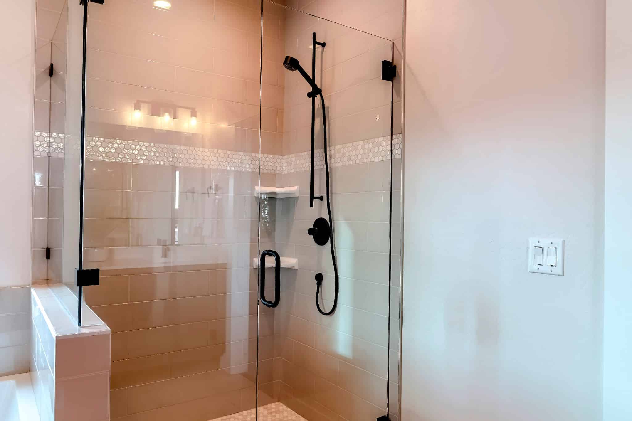 Glass walk-in shower with matte black fixtures, neutral subway tiles, and a mosaic accent line.