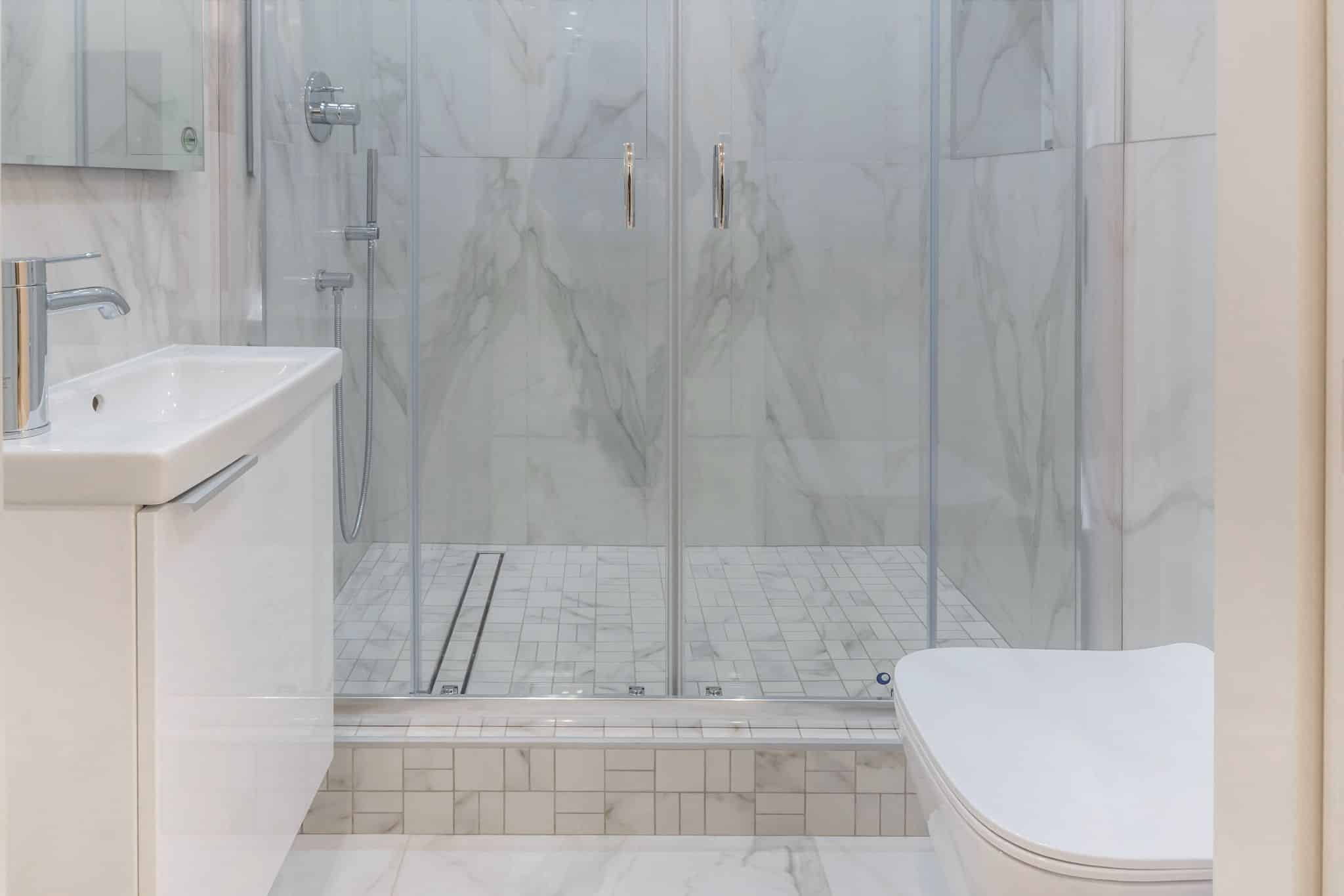 Modern bathroom with white marble tiling, glass shower doors, and a vanity sink.
