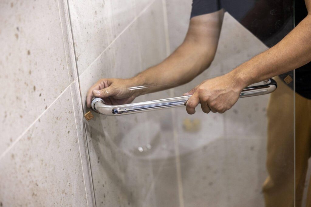 A man works on a glass door handle demonstrating repair techniques with various tools nearby