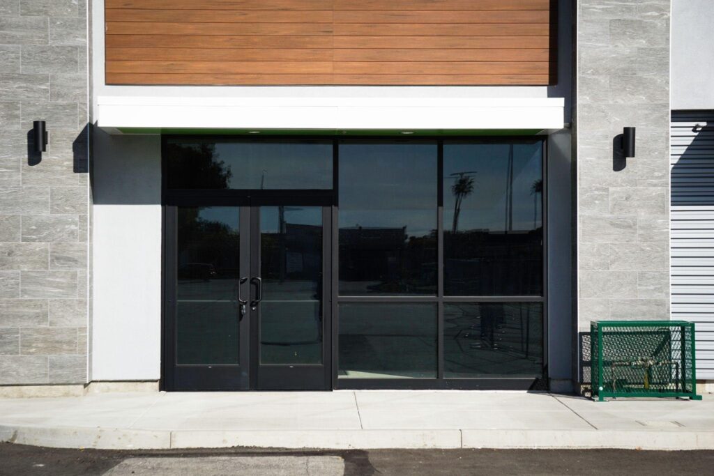 Modern commercial building entrance with dark glass double doors gray stone walls wood paneled facade