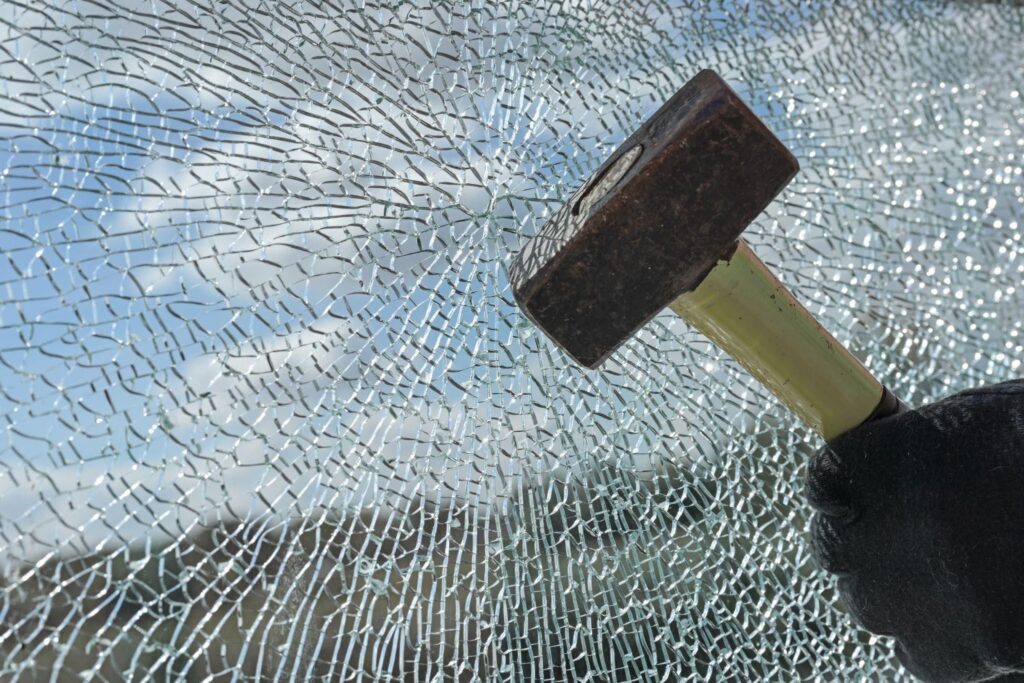 A hammer striking a glass window causing it to shatter into numerous fragments